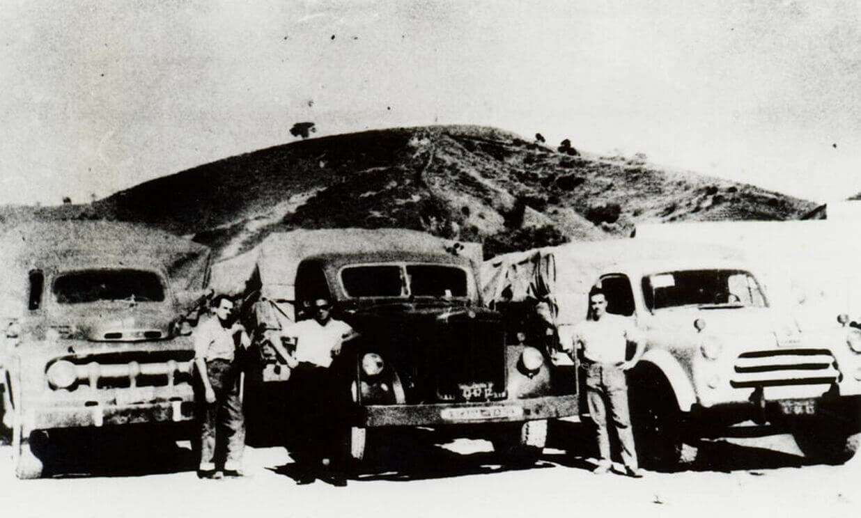 Três pessoas a frente de caminhões em foto dos anos 50